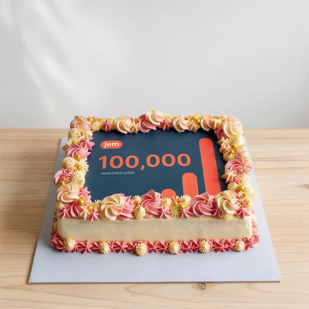 Square cake with blue edible image celebrating 100,000 registered users, decorated with pink and yellow piped frosting and…