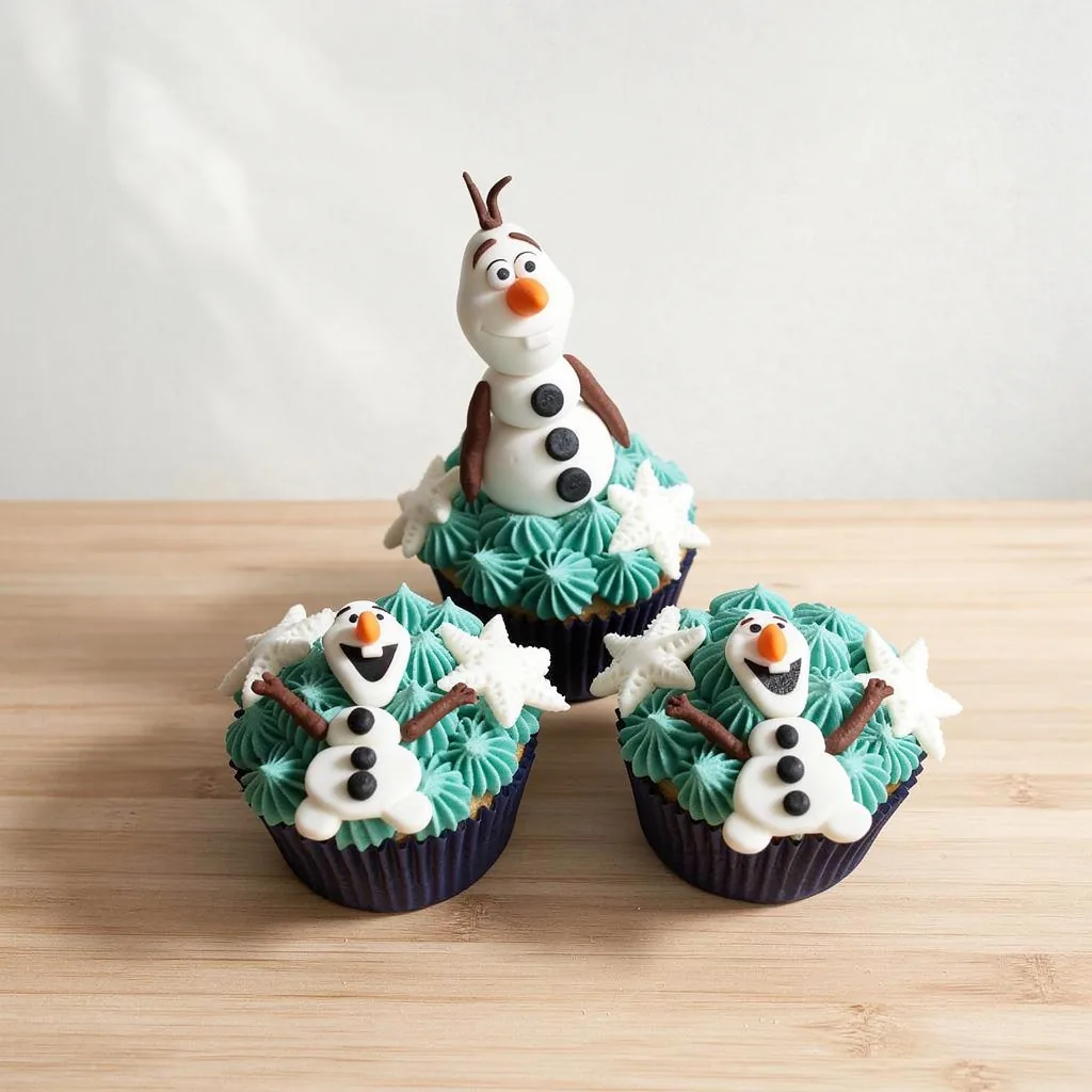 Three cupcakes with teal frosting, white snowflake decorations, and fondant snowman toppers