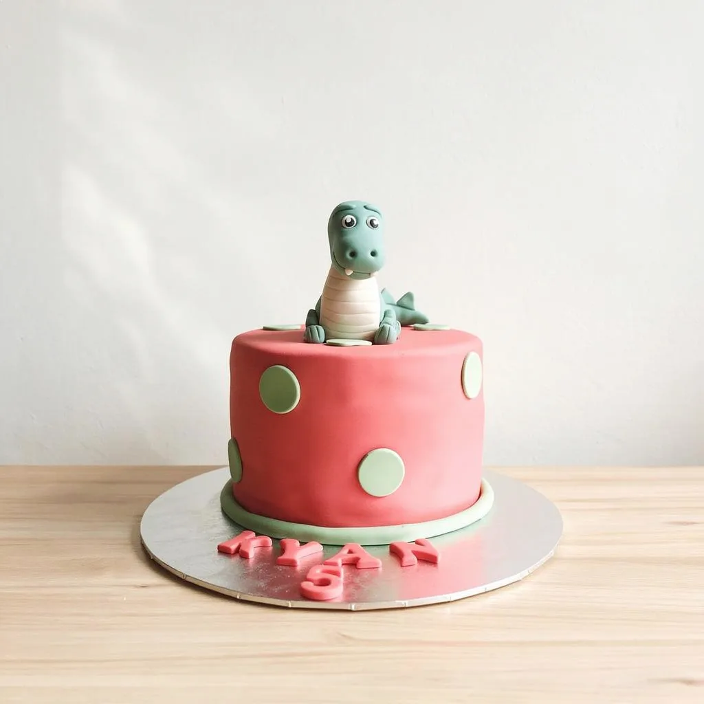 Pink round cake with green polka dots and a green dinosaur figure on top